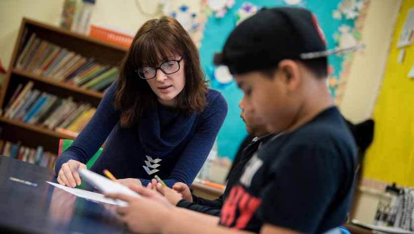 Female teacher talks with a young student in a classroom