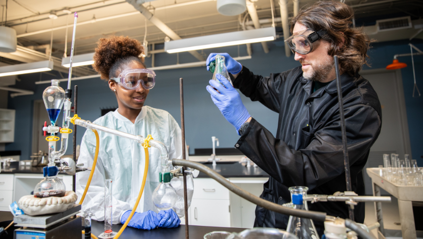 Female student wearing a white lab coat in a lab with a male professor