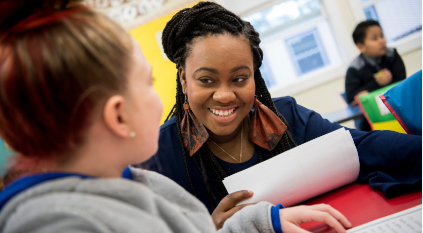 Female teacher smiles at a young student in a classroom