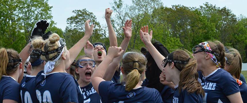 Female student lacrosse players wearing Navy blue uniforms cheer together in a huddle