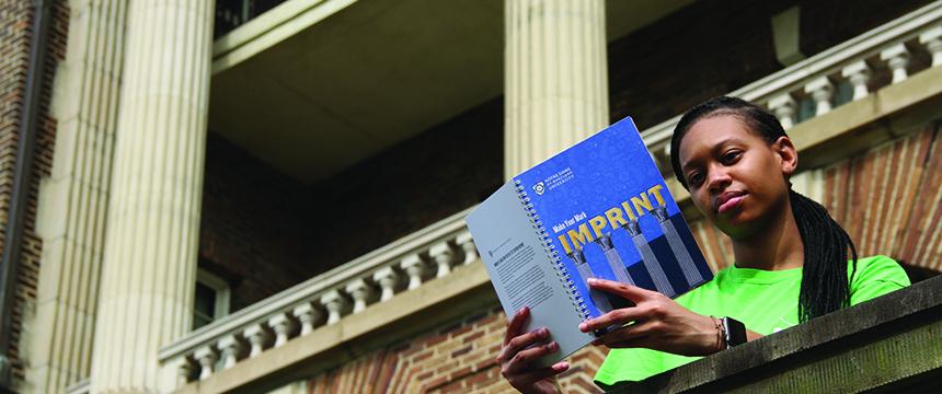 Female student reads IMPRINT book while standing on a balcony