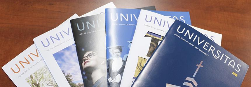 Six Universitas copies fanned out on a brown tabletop