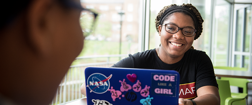 Student at a laptop with stickers such as NASA and Girls who Code