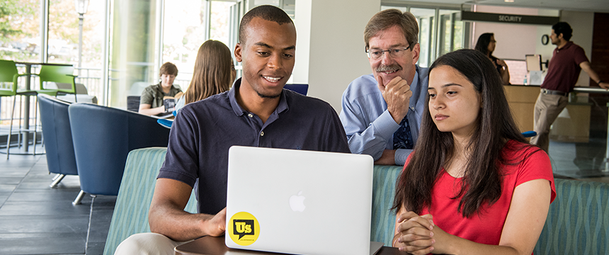 Male and female student with a teacher looking at a laptop