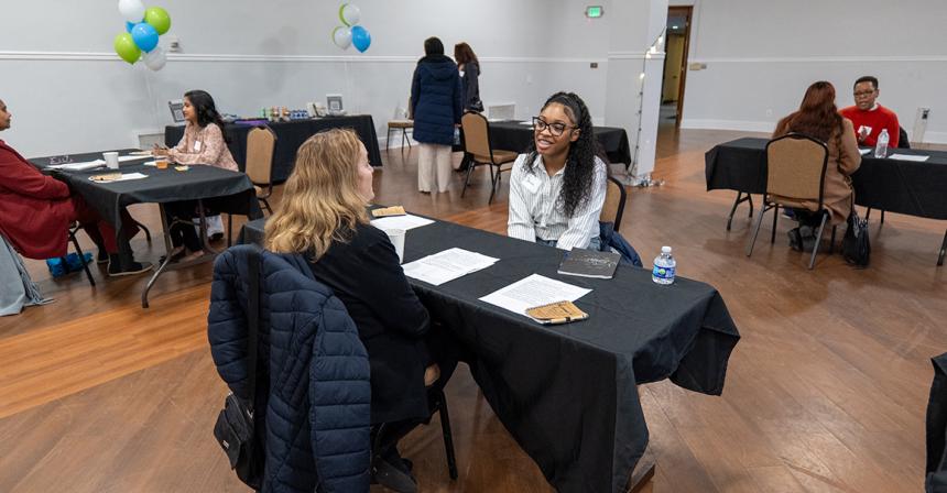 Female student smiling while sitting at a table across from another person