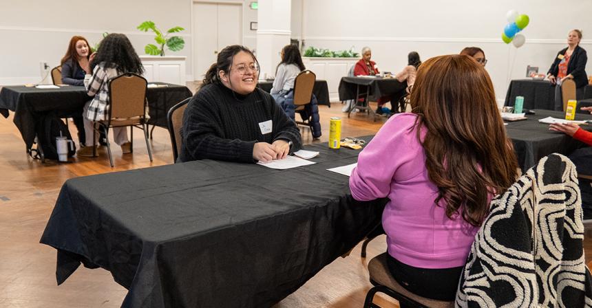 Female student smiling while sitting at a table across from another person
