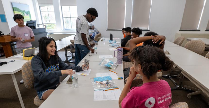 Female student wearing NDMU shirt smiles as she sits at a table across from a child