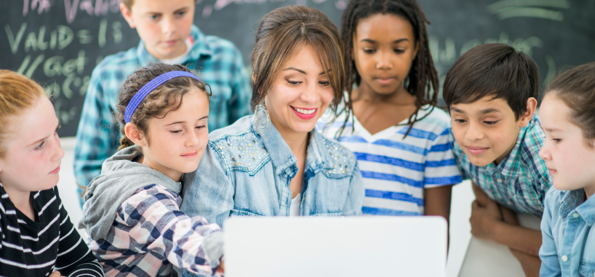 Diverse group of young students crowded around a computer screen with their teacher