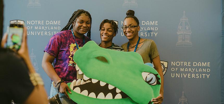 3 students holding a gator poster getting their photo taken
