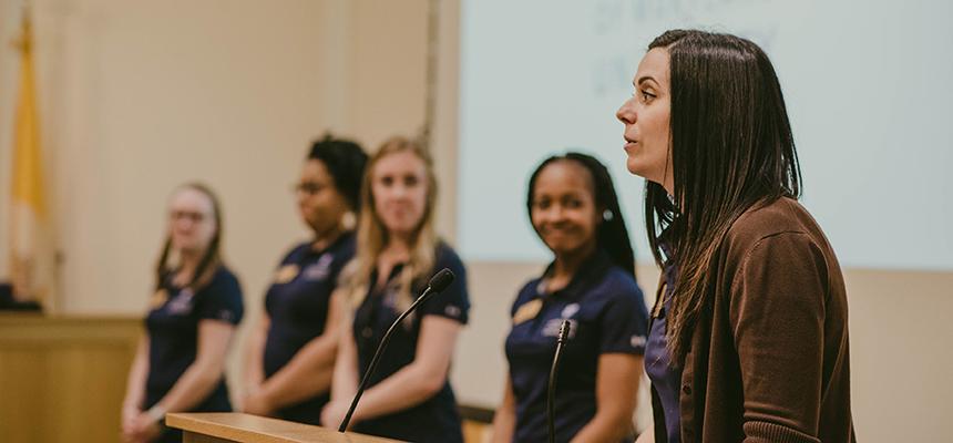 Director presents at a podium with four admissions counselors standing beside her