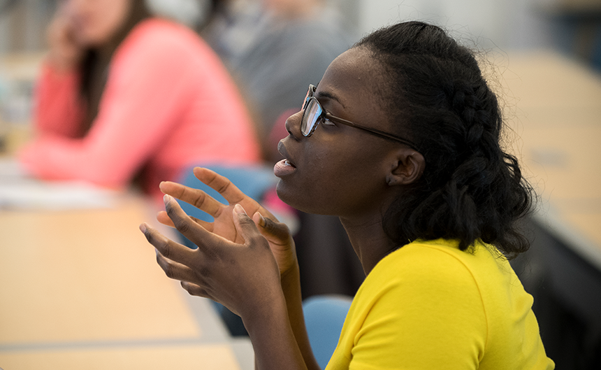 Student wearing yellow shirt asking a question and explaining with her hands