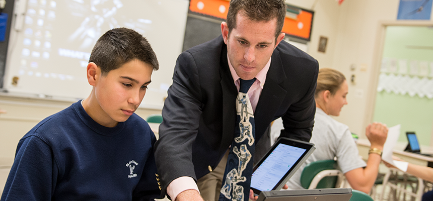 Male teacher assisting a student on a laptop