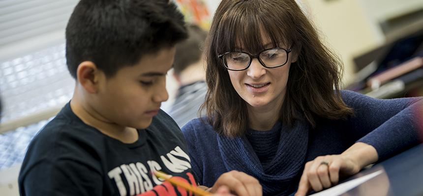 Teacher kneeling next to a student reading