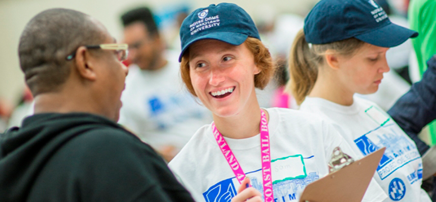 Student in hat with clipboard helping community member