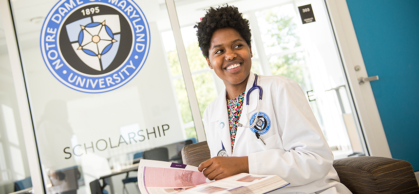 Nurse sitting at a desk with the NDMU seal in the background