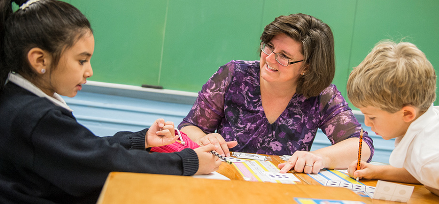 Teacher kneeling next to a desk with two students