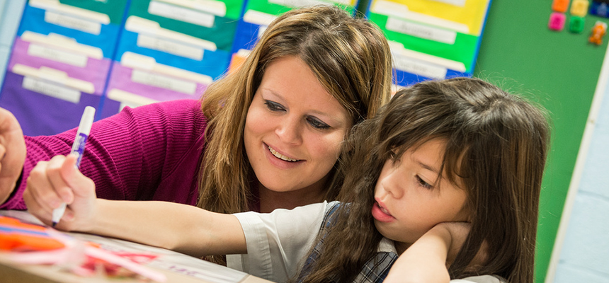 Teacher leaning next to a student helping her write