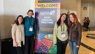 Four NDMU students and faculty pose in front of a welcome sign at the AERA conference