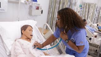 Female wearing blue nursing scrubs checks temperature on mannikin in a nursing simulation lab